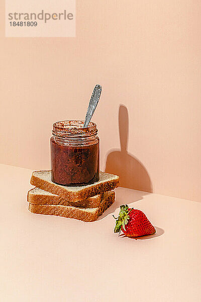 Hausgemachte Erdbeermarmelade mit Brotscheiben vor Pfirsichhintergrund