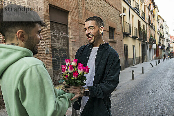 Glücklicher schwuler Mann  der seinem Freund auf der Straße Blumen schenkt