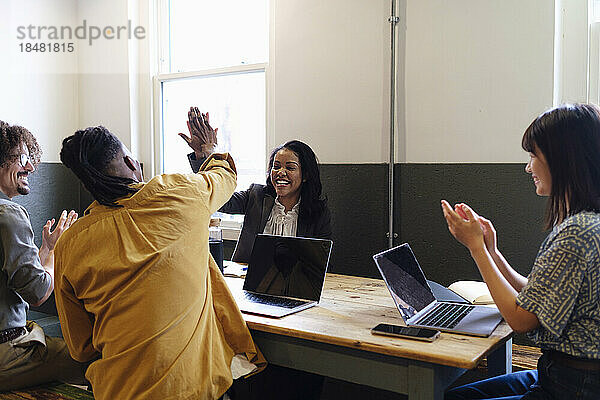 Zufriedene Geschäftskollegen geben High-Five am Schreibtisch im Büro