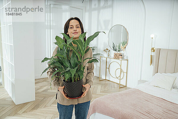 Frau mit Topfpflanze steht zu Hause im Schlafzimmer