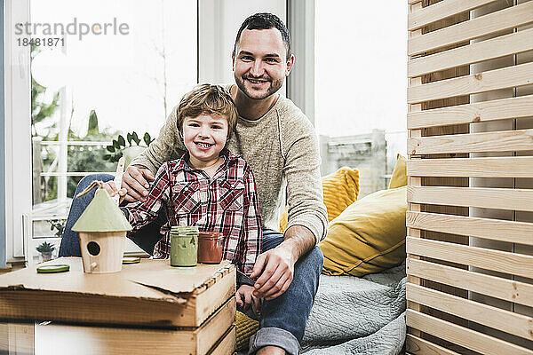 Lächelnder Vater und Sohn mit Musterhaus zu Hause