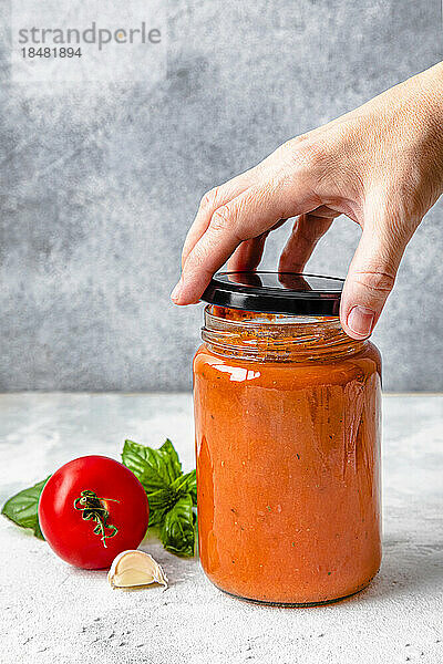 Hand einer Frau  die den Deckel eines Tomatensaucenglases öffnet