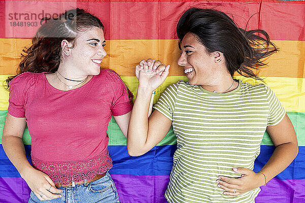 Happy lesbian couple holding hands lying on rainbow colored flag
