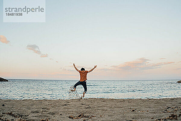 Sorgloser Mann springt bei Sonnenuntergang vor das Meer