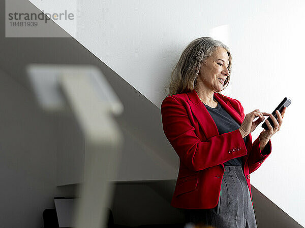 Lächelnde ältere Geschäftsfrau  die im Büro ihr Smartphone benutzt