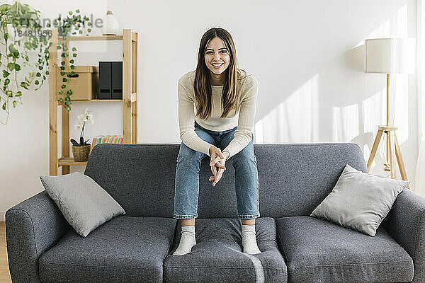Glückliche junge Frau sitzt auf dem Sofa im Wohnzimmer