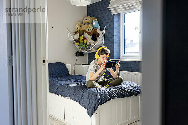 Junge mit Kopfhörern spielt zu Hause im Schlafzimmer ein Videospiel auf einem Tablet-PC