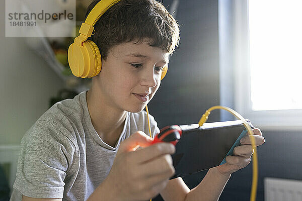 Lächelnder Junge mit Kopfhörern  der ein Videospiel auf einem Tablet-PC spielt