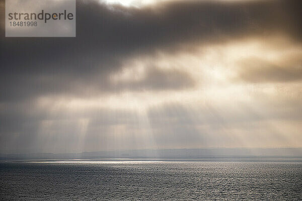 Sunbeams falling on sea through storm clouds at sunset