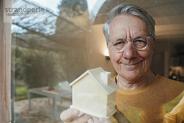 Lächelnder Mann mit Musterhaus durch Glas gesehen