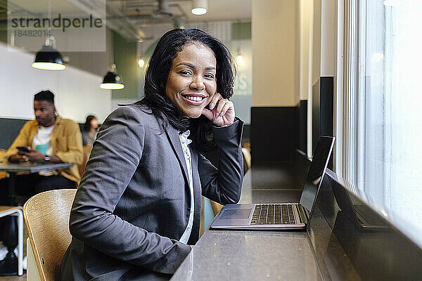 Lächelnde Geschäftsfrau mit Laptop auf dem Tisch am Arbeitsplatz