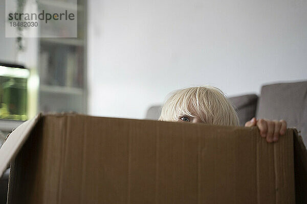 Boy peeking from cardboard box at home
