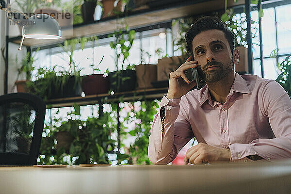 Reifer Geschäftsmann  der im Büro sitzt und am Smartphone spricht