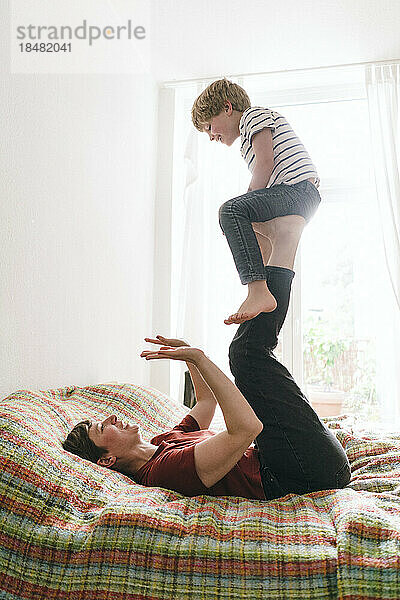 Mother playing with son lying on bed at home