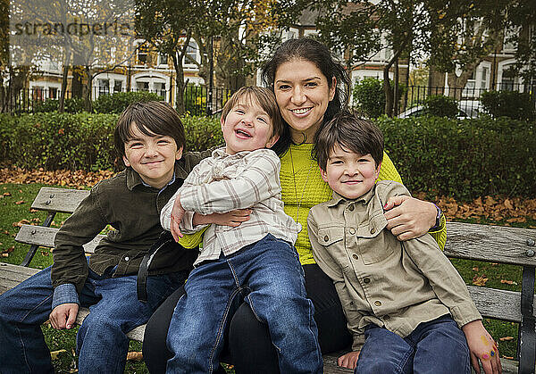 Smiling woman sitting with boys on bench at park
