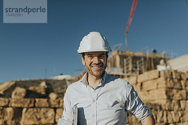 Glücklicher Architekt mit Bauarbeiterhelm  der auf der Baustelle steht