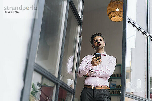 Nachdenklicher reifer Geschäftsmann mit Smartphone im Büro