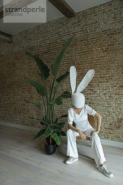 Frau sitzt auf einem Stuhl und trägt eine Kaninchenmaske