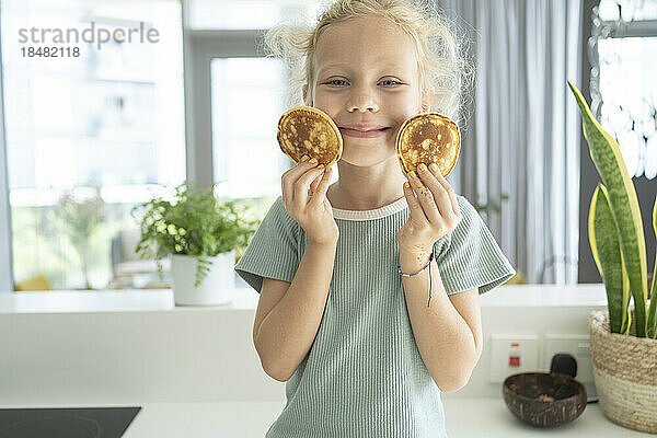 Smiling girl holding pancakes in kitchen at home