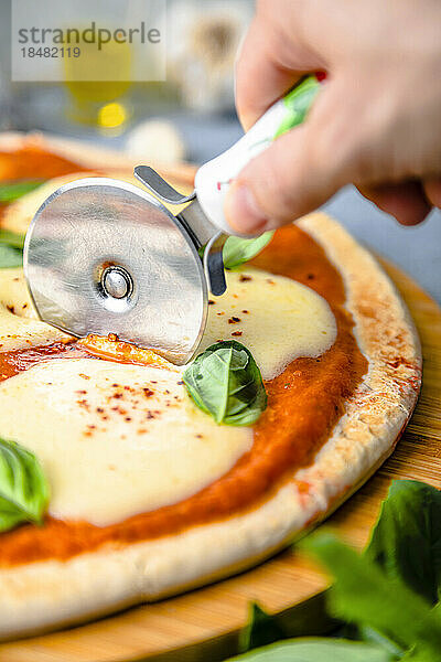 Hand einer Frau  die Pizza mit einem Cutter auf dem Tisch schneidet