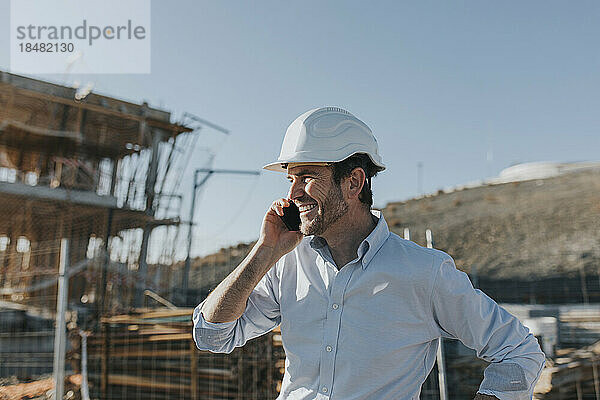 Glücklicher reifer Architekt  der auf der Baustelle mit dem Smartphone spricht
