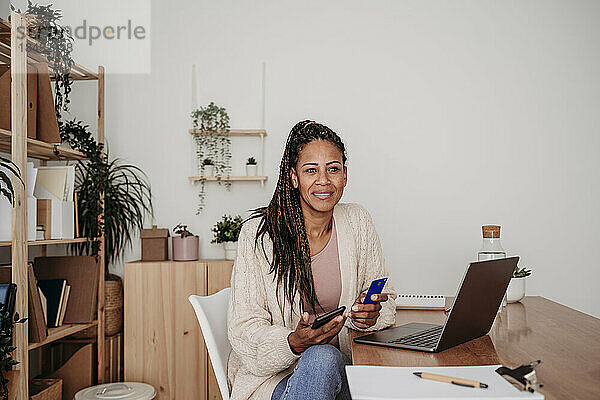 Lächelnder Freiberufler mit Kreditkarte und Smartphone im Heimbüro
