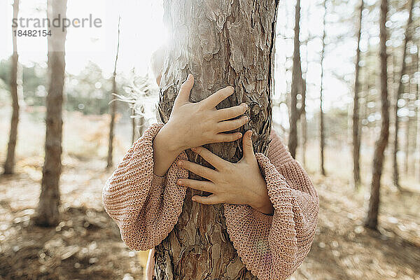 Mädchen umarmt Baumstamm im Wald