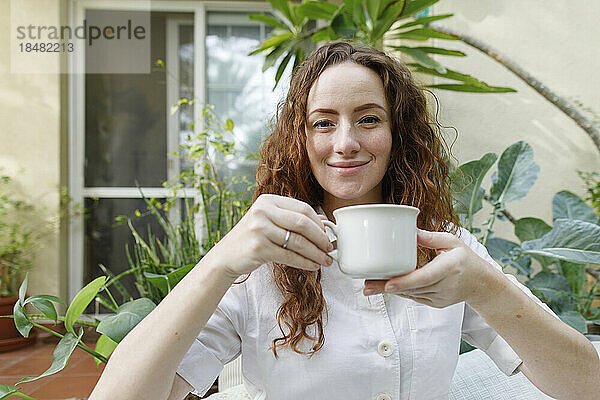Lächelnde Frau trinkt eine Tasse Tee im Hinterhof