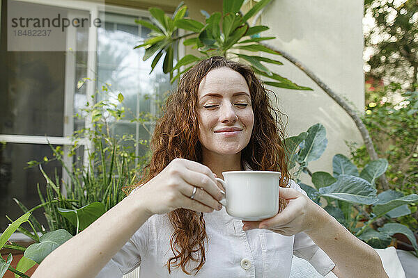 Lächelnde Frau genießt eine Tasse Tee im Hinterhof