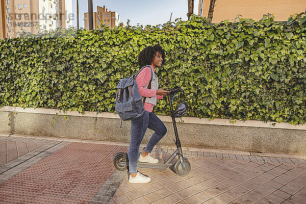 Junge Frau mit Elektroroller steht auf Fußweg