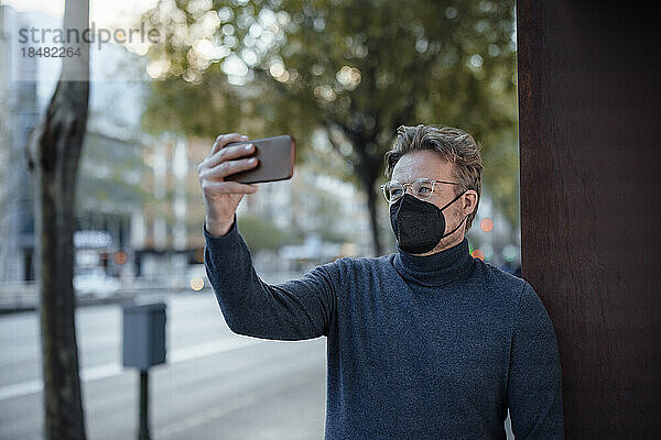 Mann mit schützender Gesichtsmaske macht Selfie mit Smartphone