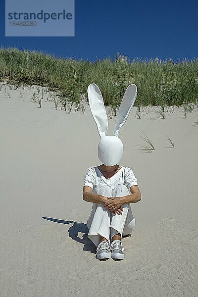 Woman with rabbit mask sitting on sand dune