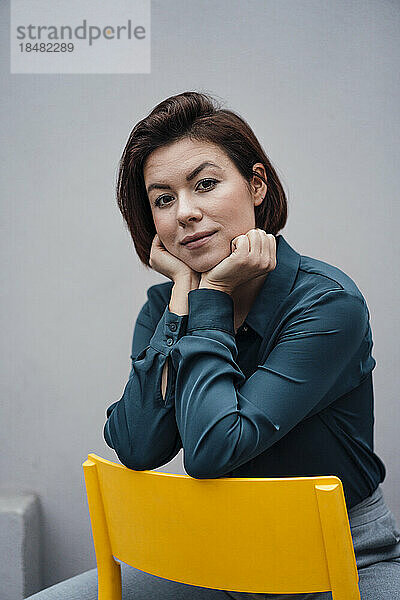 Selbstbewusste junge Geschäftsfrau sitzt auf einem Stuhl vor der Wand