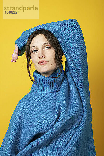 Confident young woman wearing blue turtleneck over yellow background