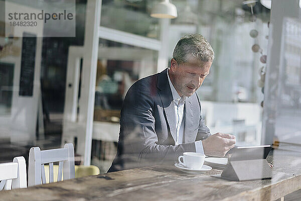 Geschäftsmann frühstückt und nutzt Tablet-PC im Café