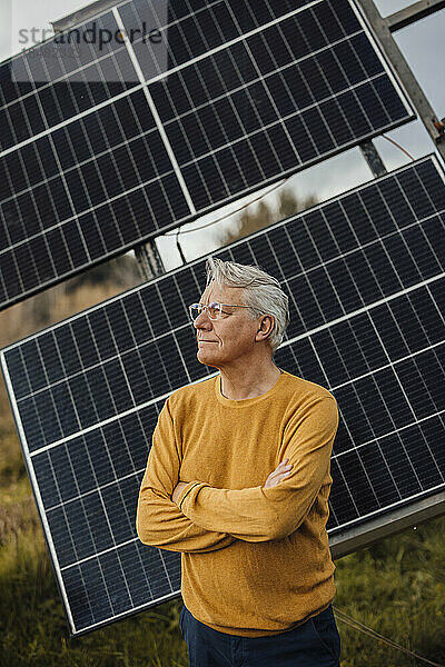 Älterer Mann steht mit verschränkten Armen vor Sonnenkollektoren