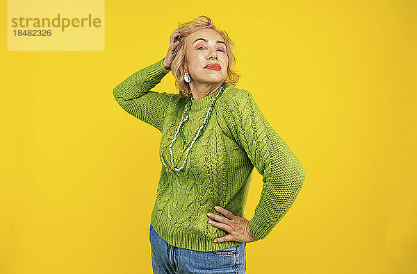 Selbstbewusste ältere Frau steht vor gelbem Hintergrund