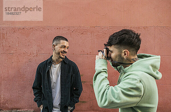 Man clicking photos of friend in front of wall