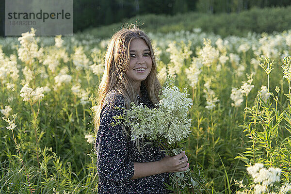 Smiling young woman holding bouquet of flowers standing in field