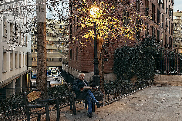 Älterer Mann liest Buch und sitzt neben Laternenpfahl