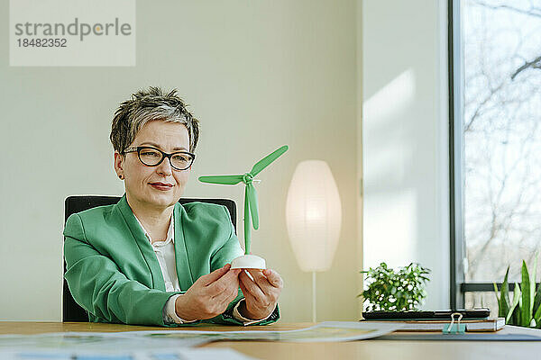 Reife Geschäftsfrau blickt im Büro auf eine Windkraftanlage