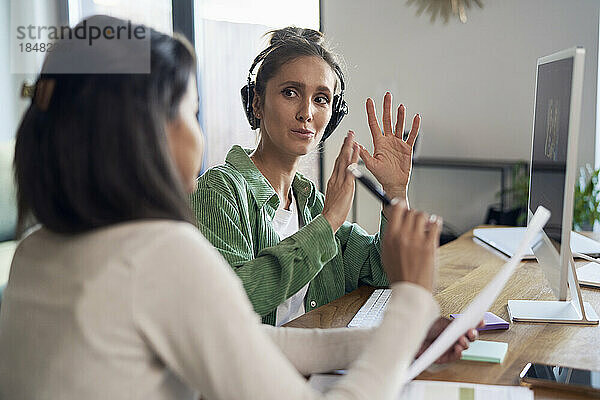 Geschäftsfrau mit Kopfhörer erklärt Kollege im Homeoffice