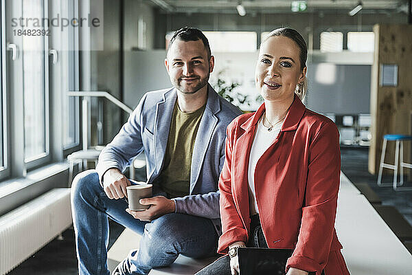 Lächelnde Geschäftskollegen sitzen am Schreibtisch im Büro