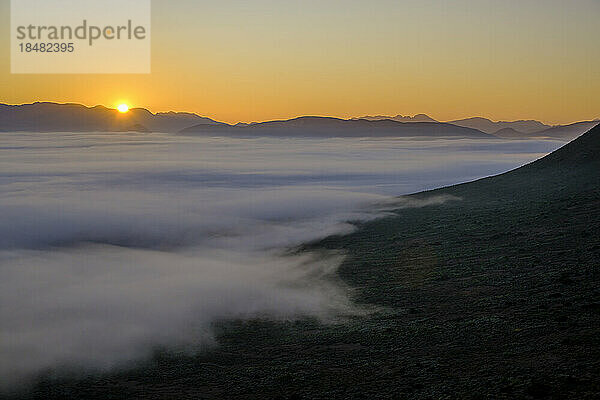 Scenic view of mountains with fog at sunrise