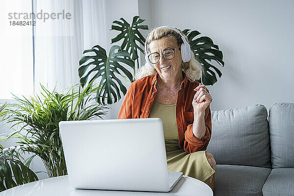 Lächelnde Frau  die zu Hause Musik über Kopfhörer und Laptop genießt