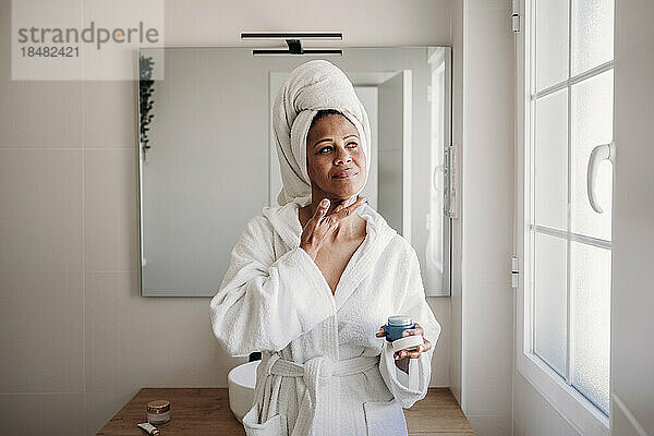 Frau trägt im Badezimmer Feuchtigkeitscreme auf ihr Gesicht auf
