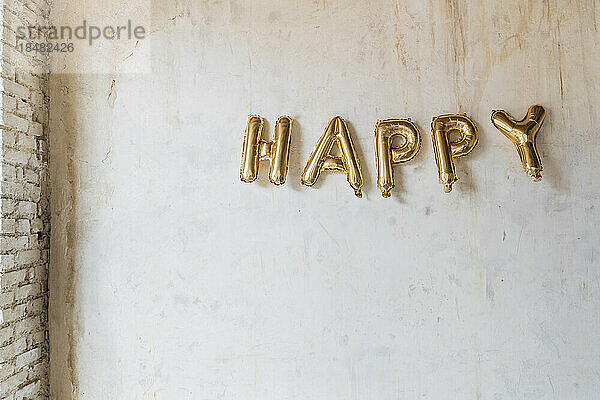 Gold colored happy text made with inflated balloons hanging on wall