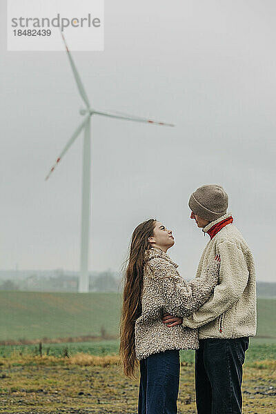 Teenager-Paar steht zusammen vor einer Windkraftanlage