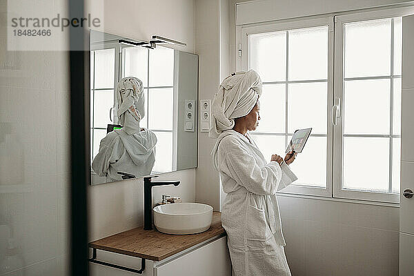 Reife Frau benutzt Tablet-PC im Badezimmer zu Hause
