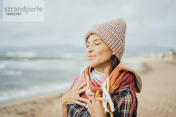 Lächelnde Frau mit den Händen auf der Brust am Strand